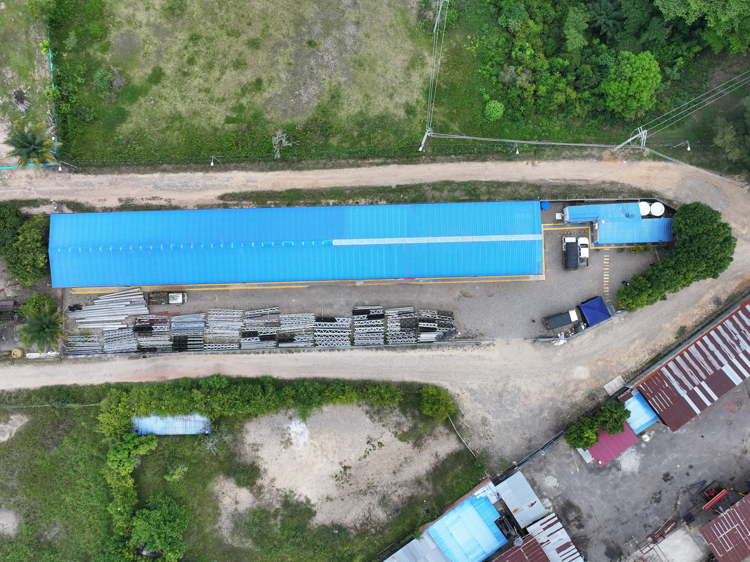 Vista aérea cenital del lote: hangar de cubierta azul, patio de almacenamiento con estructuras metálicas, área administrativa y cerramiento perimetral