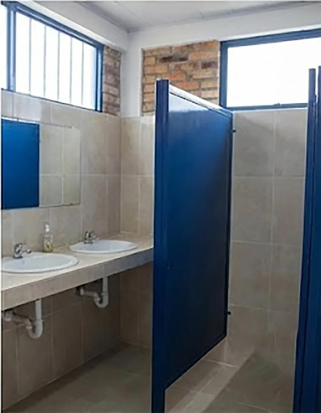 Batería de baños con enchape cerámico, divisiones metálicas azules y lavamanos