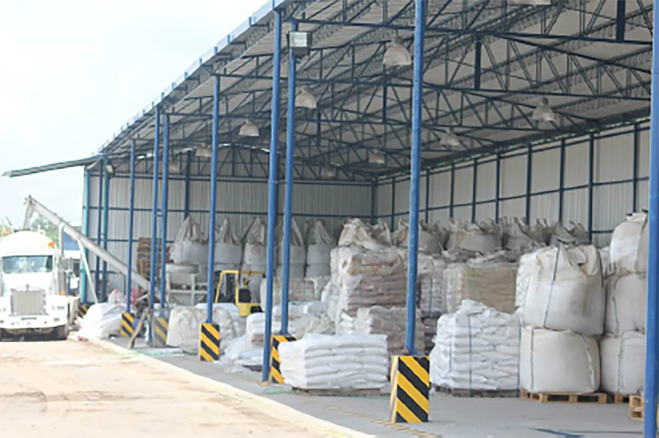 Interior del hangar: pórticos metálicos azules, cerchas de cubierta, iluminación industrial y carga paletizada almacenada